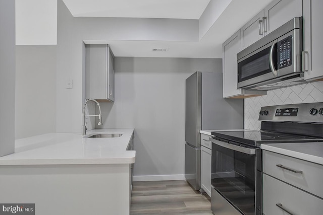 kitchen with a sink, stainless steel appliances, gray cabinets, and decorative backsplash