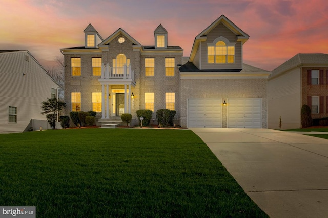 colonial inspired home featuring brick siding, concrete driveway, a lawn, a balcony, and an attached garage