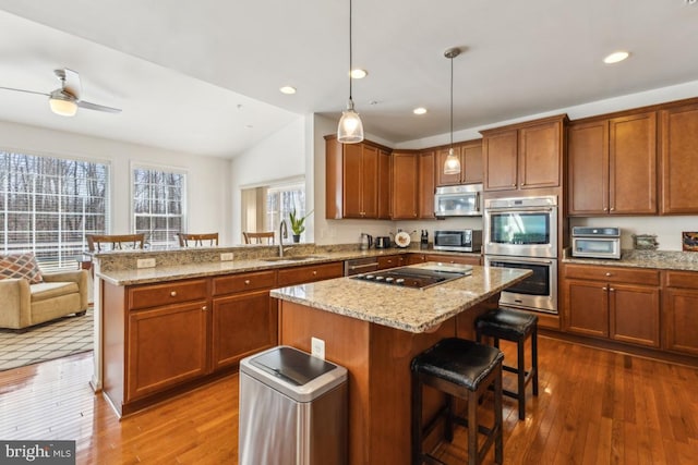 kitchen featuring hardwood / wood-style flooring, a sink, a kitchen breakfast bar, appliances with stainless steel finishes, and a peninsula