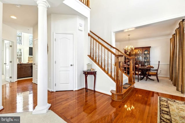 stairs featuring a notable chandelier, wood finished floors, baseboards, and ornate columns