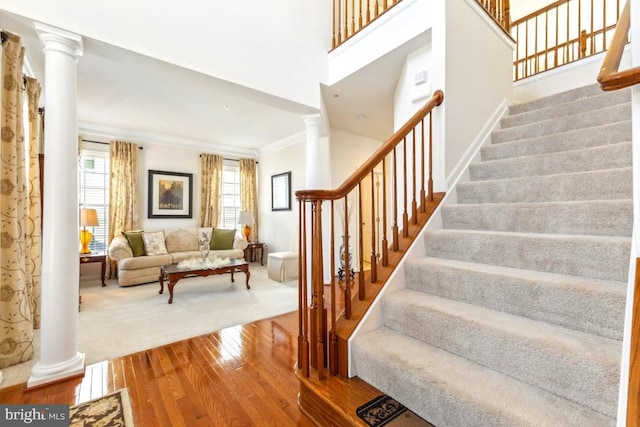 stairway featuring hardwood / wood-style flooring, crown molding, a towering ceiling, and decorative columns