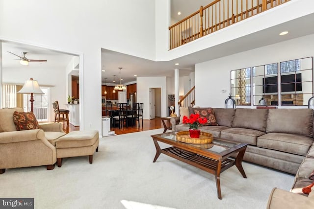 living area featuring stairs, light carpet, recessed lighting, ceiling fan with notable chandelier, and a high ceiling