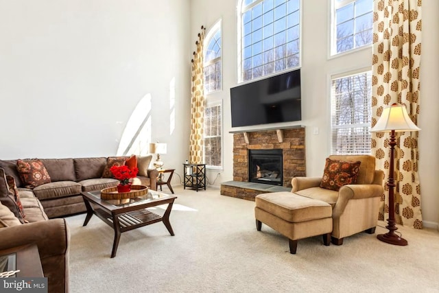 living room featuring a stone fireplace, baseboards, a high ceiling, and carpet