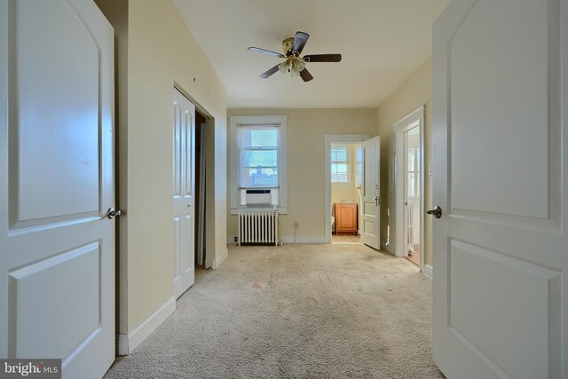 unfurnished bedroom featuring ensuite bathroom, cooling unit, light colored carpet, baseboards, and radiator heating unit