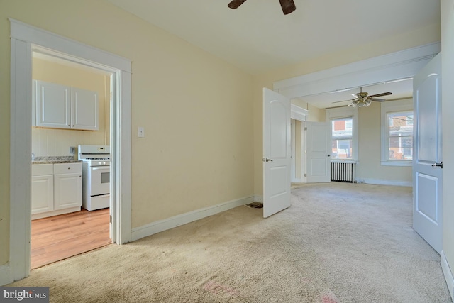 unfurnished room with radiator, ceiling fan, baseboards, and light colored carpet