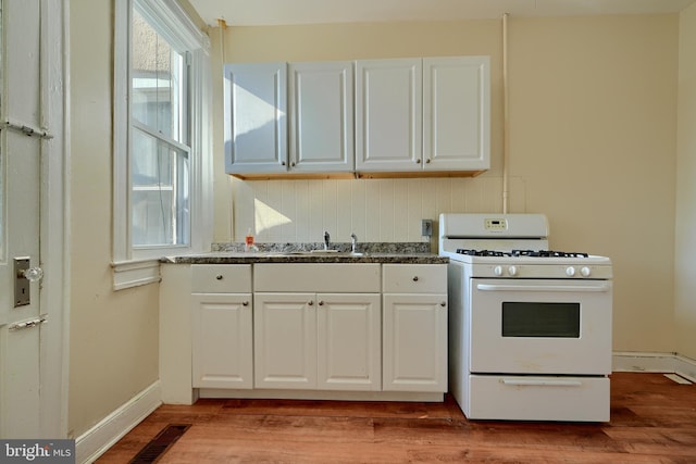 kitchen with a sink, light wood finished floors, white cabinets, and gas range gas stove