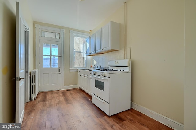 kitchen with tasteful backsplash, baseboards, radiator heating unit, wood finished floors, and white gas range