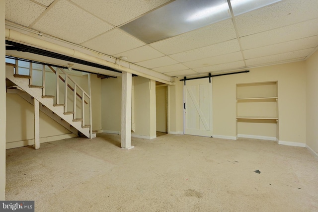 finished basement with a drop ceiling, stairway, baseboards, and a barn door