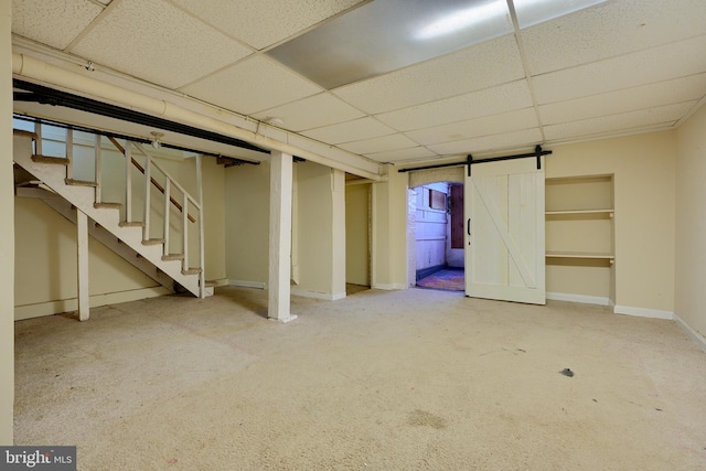 finished basement with carpet floors, stairway, a barn door, a drop ceiling, and baseboards