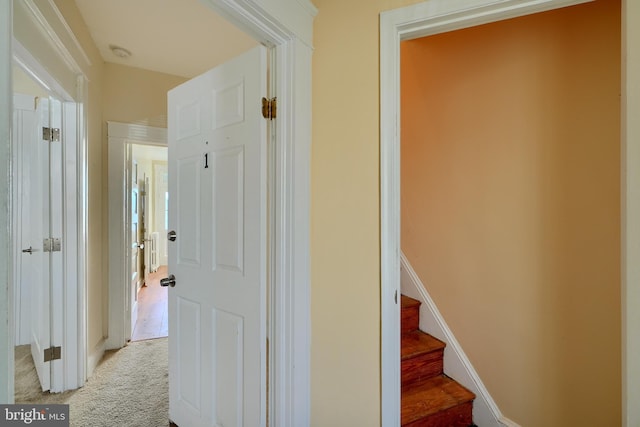 corridor with stairs, light carpet, and baseboards