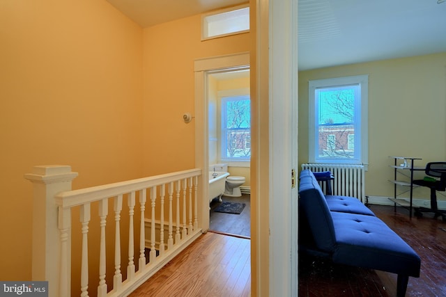 hallway with radiator heating unit, wood-type flooring, a wealth of natural light, and an upstairs landing