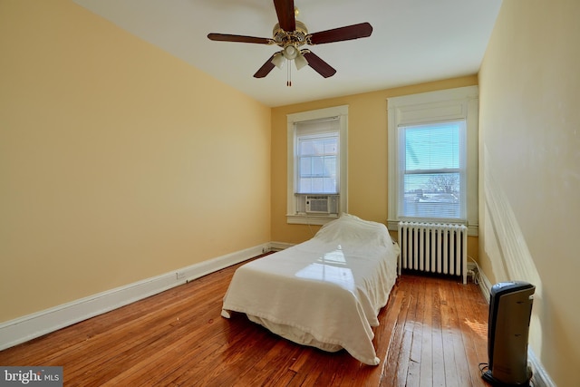 bedroom with a ceiling fan, wood-type flooring, baseboards, and radiator heating unit