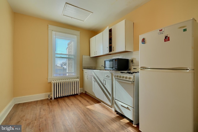 kitchen with light wood finished floors, backsplash, radiator heating unit, white cabinets, and white appliances