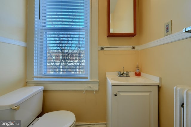 bathroom with toilet, radiator heating unit, a wealth of natural light, and vanity