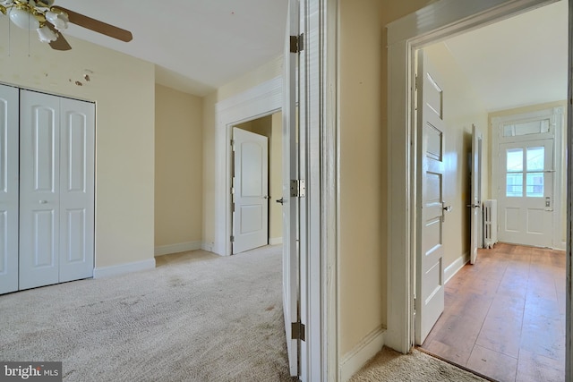 hall featuring baseboards, light wood-style flooring, and light colored carpet