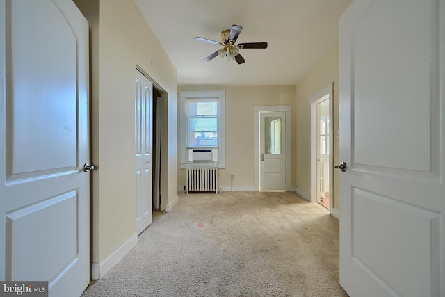 interior space featuring baseboards, light carpet, ceiling fan, and radiator heating unit