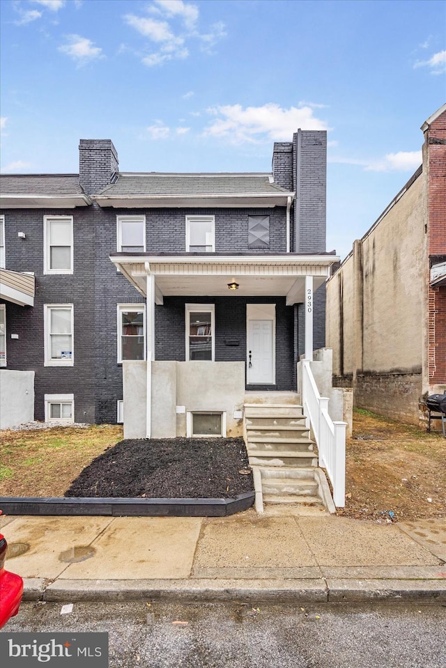 view of property featuring a chimney, a porch, and brick siding