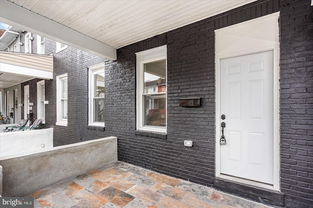 view of exterior entry with a porch and brick siding