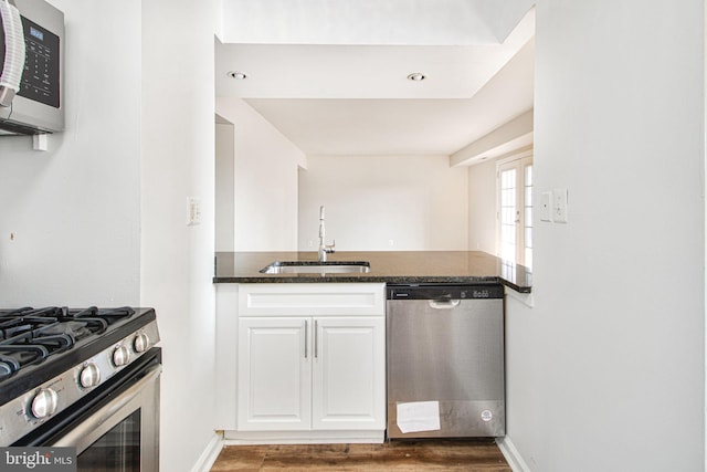 kitchen with stainless steel appliances, wood finished floors, a sink, white cabinetry, and dark stone countertops