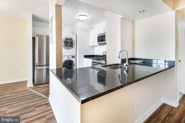 kitchen featuring stainless steel appliances, stacked washer / dryer, wood finished floors, a sink, and dark stone counters