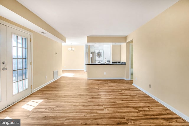 unfurnished living room featuring visible vents, light wood-style flooring, baseboards, and an inviting chandelier