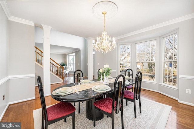 dining area featuring stairway, wood finished floors, crown molding, and ornate columns