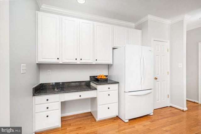 kitchen with dark stone countertops, freestanding refrigerator, ornamental molding, light wood-style floors, and white cabinetry