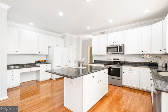 kitchen featuring light wood finished floors, built in study area, stainless steel appliances, white cabinets, and a center island