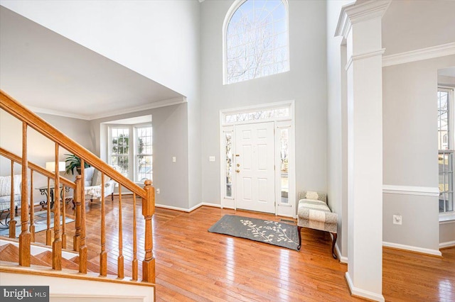 foyer entrance featuring baseboards, crown molding, ornate columns, and hardwood / wood-style floors