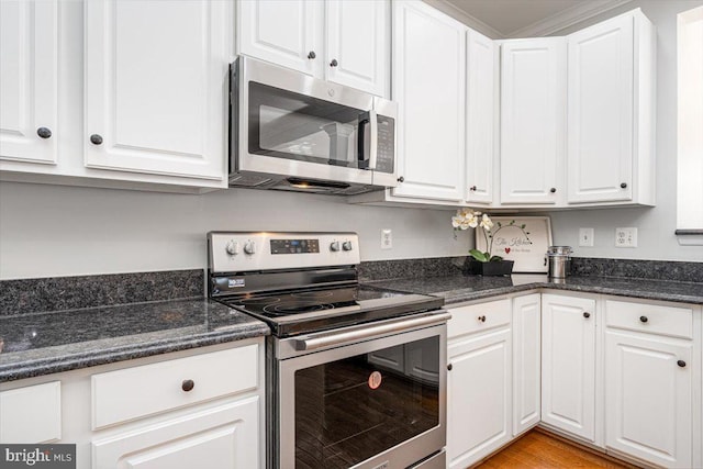 kitchen featuring white cabinetry, dark stone countertops, light wood-style flooring, and appliances with stainless steel finishes