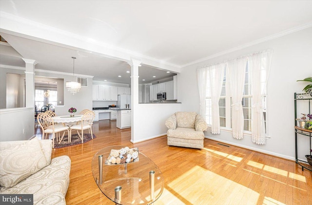 living area featuring light wood finished floors, baseboards, crown molding, and ornate columns