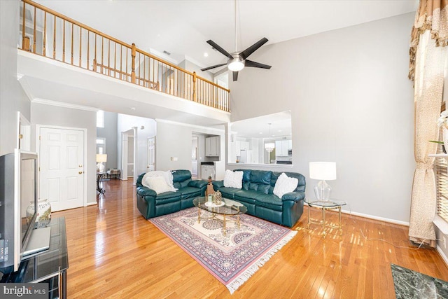 living room with a ceiling fan, a high ceiling, baseboards, and wood finished floors