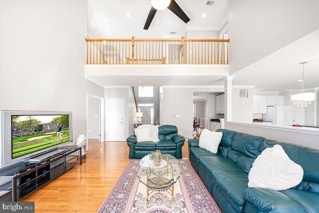 living room featuring visible vents, a high ceiling, crown molding, ceiling fan with notable chandelier, and light wood-type flooring