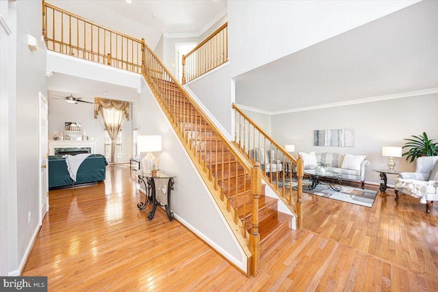 stairway featuring baseboards, a high ceiling, a fireplace, hardwood / wood-style flooring, and crown molding