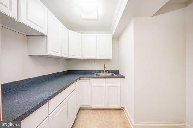 kitchen with a sink, dark countertops, white cabinets, light tile patterned floors, and baseboards