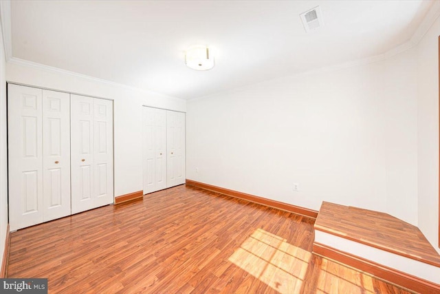 unfurnished bedroom with baseboards, multiple closets, wood finished floors, and ornamental molding