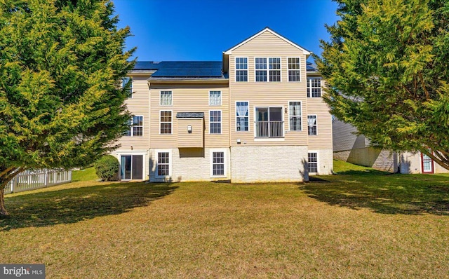 rear view of property with roof mounted solar panels, a lawn, and fence