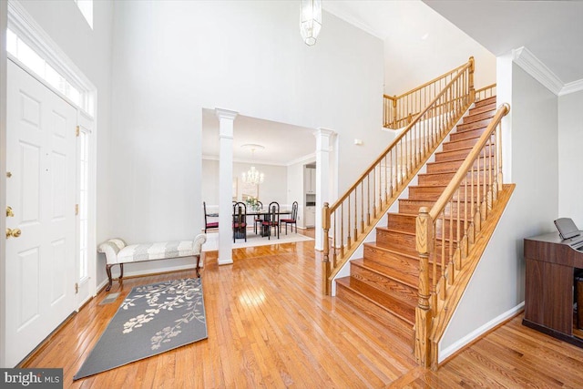 entrance foyer featuring crown molding, stairs, a towering ceiling, hardwood / wood-style flooring, and ornate columns