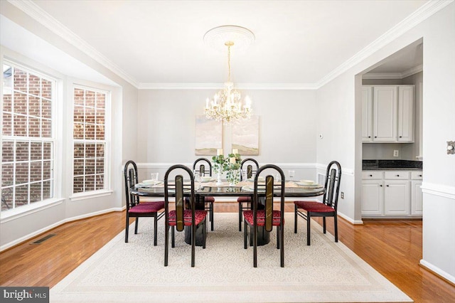 dining room with visible vents, a notable chandelier, light wood-style flooring, and ornamental molding