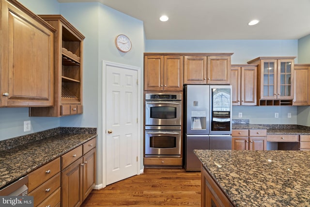 kitchen featuring dark wood-type flooring, dark stone countertops, recessed lighting, appliances with stainless steel finishes, and glass insert cabinets