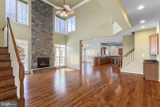 unfurnished living room featuring a stone fireplace, dark wood-type flooring, stairway, and a wealth of natural light