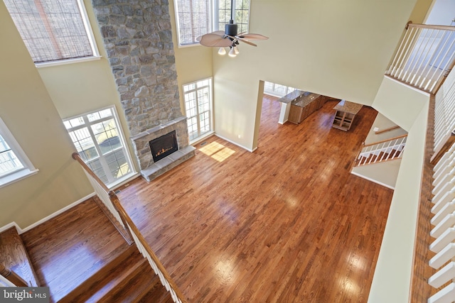 unfurnished living room featuring stairway, a stone fireplace, a towering ceiling, wood finished floors, and a ceiling fan