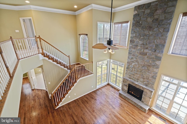 living area with a stone fireplace, crown molding, a high ceiling, and wood finished floors