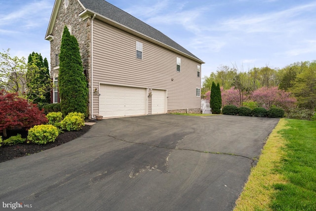 view of property exterior featuring a garage, stone siding, and driveway