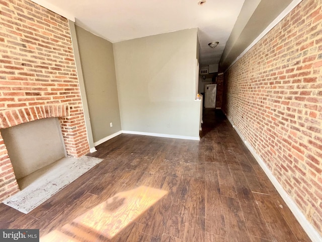 unfurnished living room with brick wall, baseboards, a fireplace, and hardwood / wood-style floors