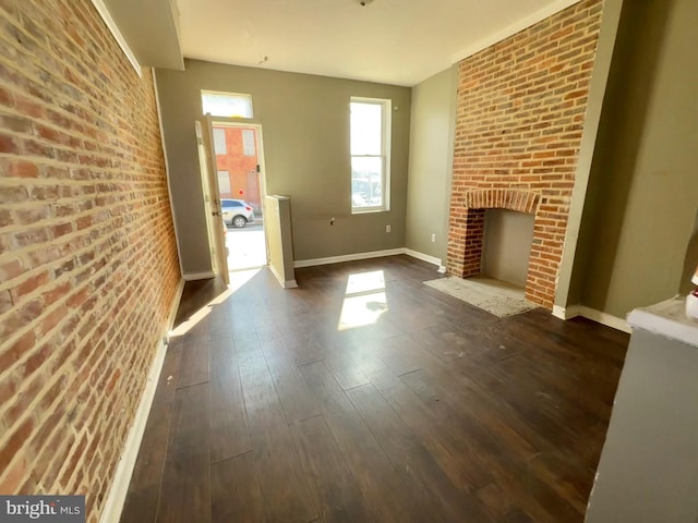 unfurnished living room featuring a brick fireplace, dark wood-style flooring, brick wall, and baseboards