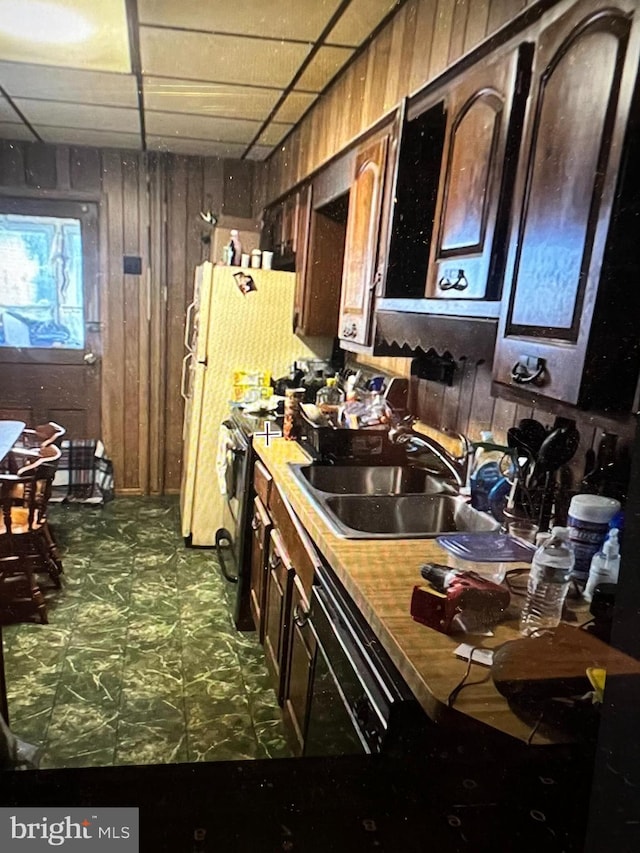 kitchen featuring black electric range oven, a sink, wooden walls, dark floors, and a paneled ceiling