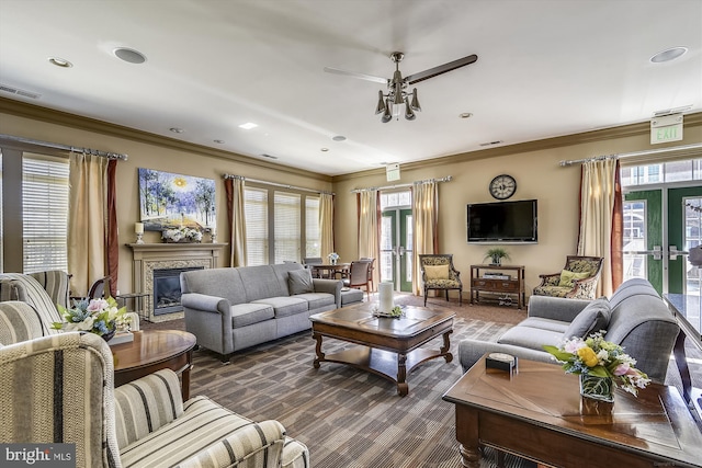 living area with french doors, a glass covered fireplace, visible vents, and crown molding