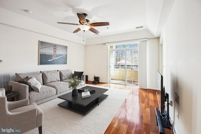 living room with wood-type flooring, visible vents, ceiling fan, and baseboards