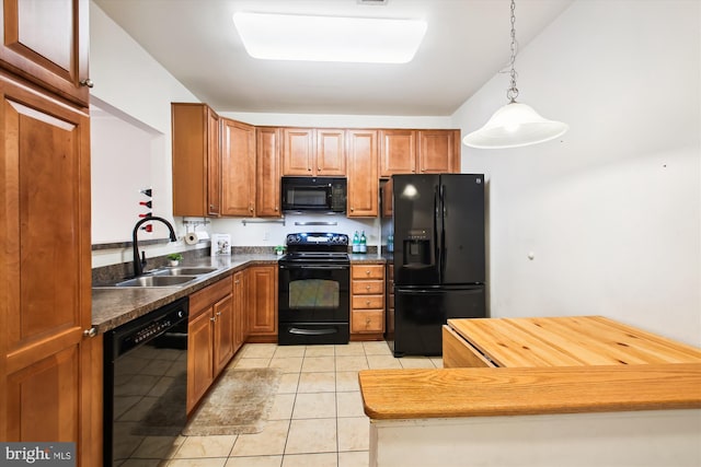 kitchen with light tile patterned floors, hanging light fixtures, brown cabinetry, a sink, and black appliances